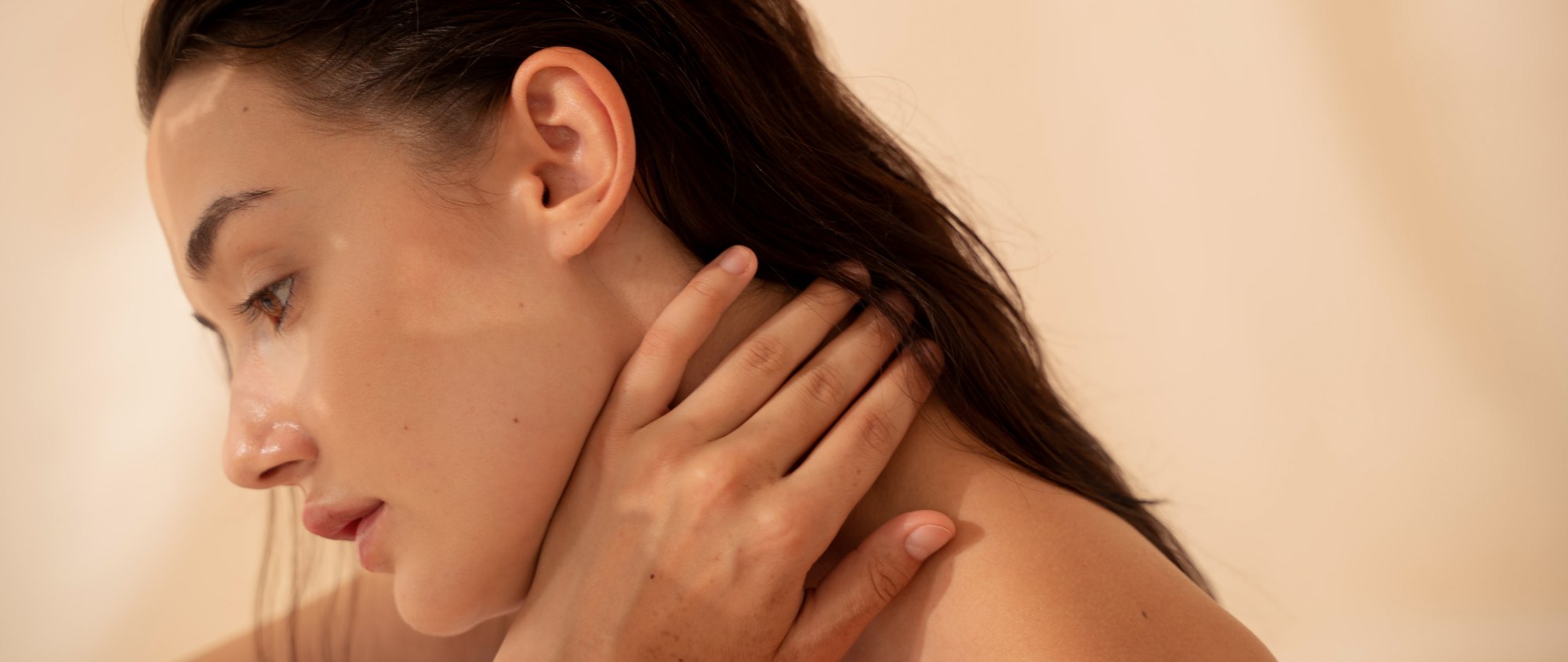 Junge Frau mit gesunder Haut und glänzendem Haar berührt sanft ihren Nacken.