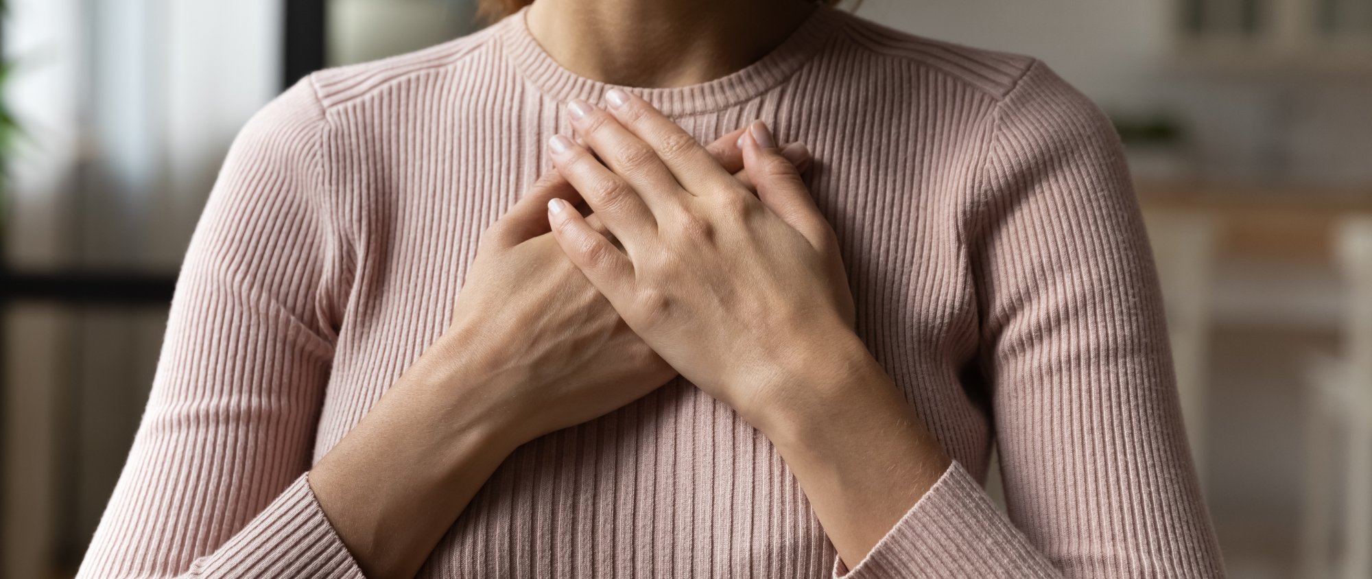 Frau legt beide Hände auf ihre Brust.