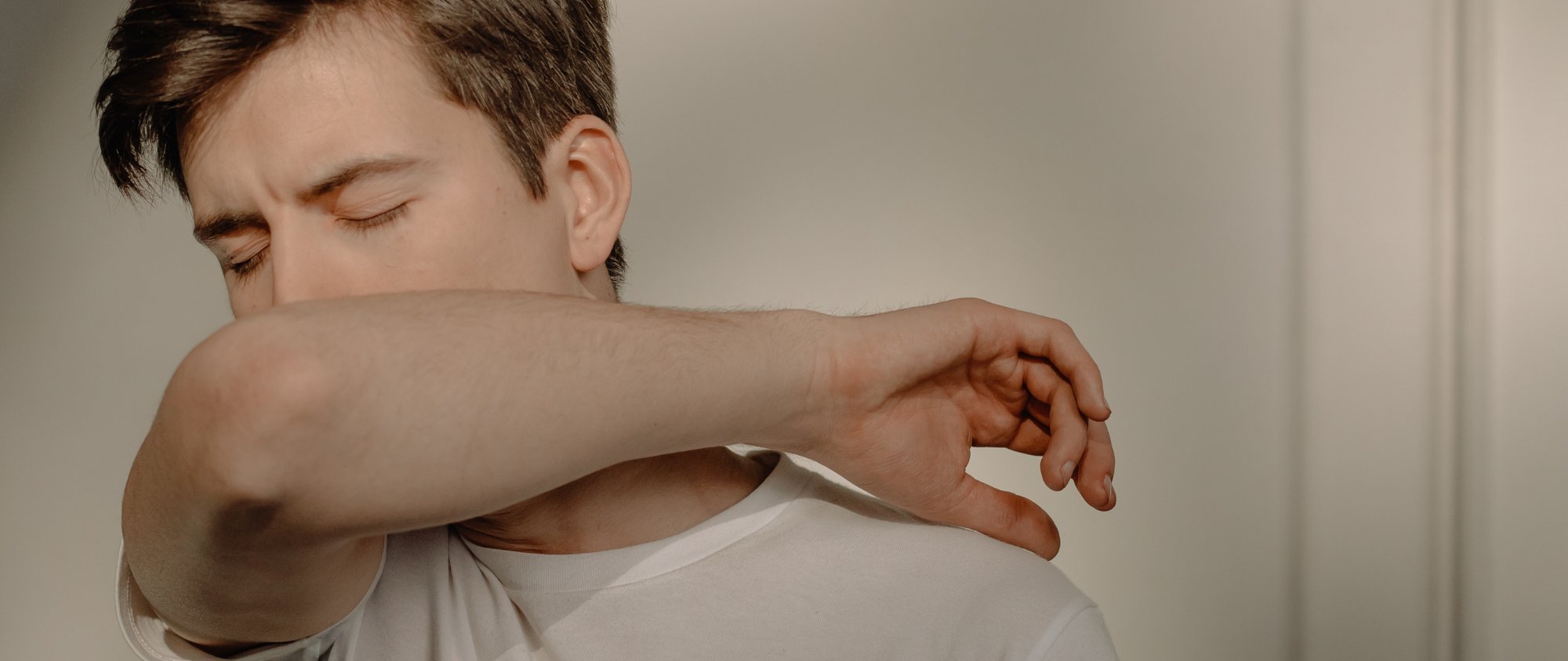 Junger Mann niest in seine Armbeuge, um die Ausbreitung von Keimen zu vermeiden.