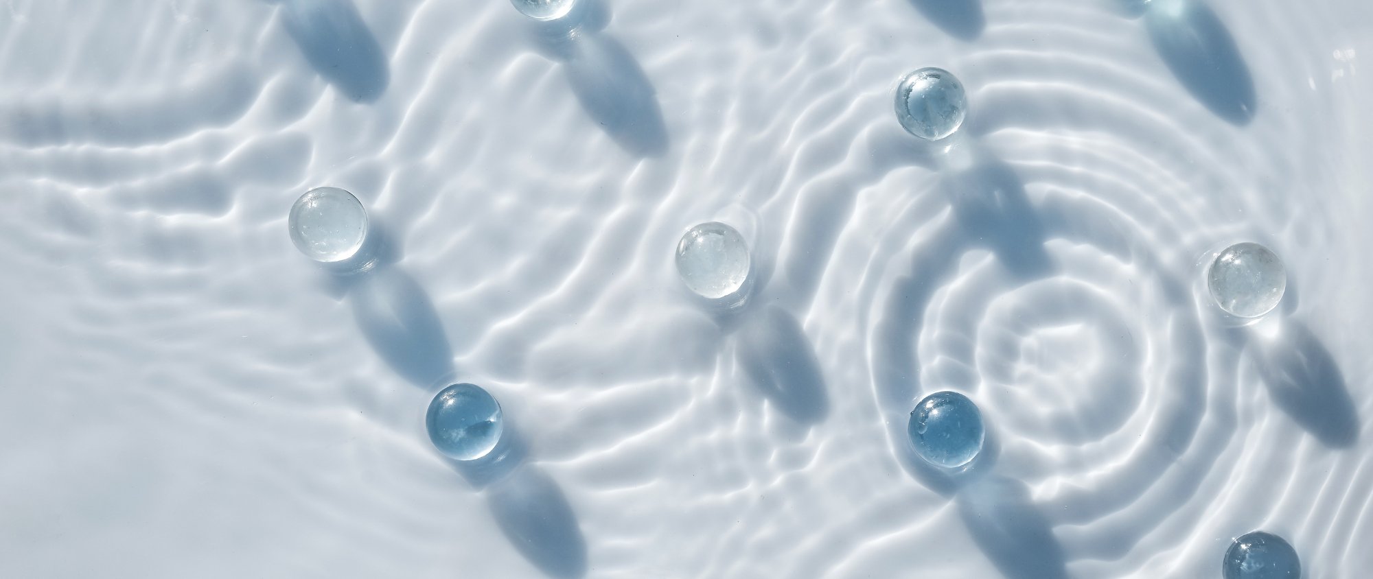 Transparente Gelkugeln auf Wasseroberfläche mit Lichtreflexionen.