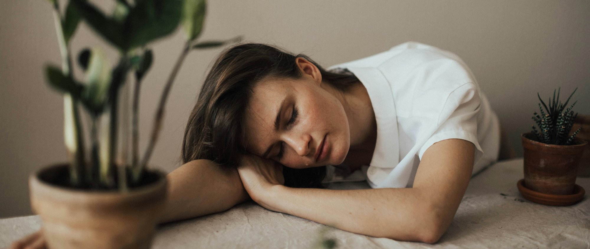 Erschöpfte Frau mit geschlossenen Augen lehnt mit dem Kopf auf dem Tisch.