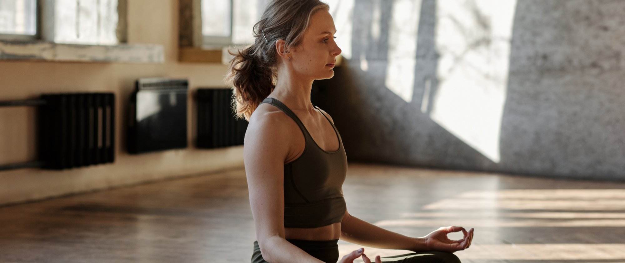 Frau meditiert im Schneidersitz in einem hellen Raum.