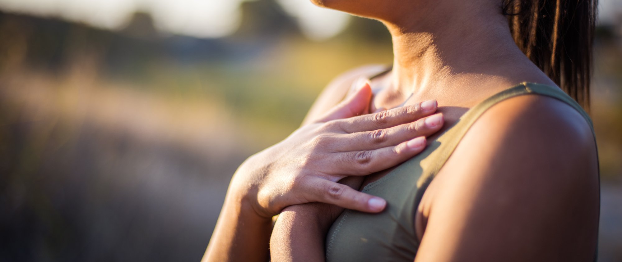 Frau legt achtsam beide Hände auf ihre Brust im Sonnenlicht.