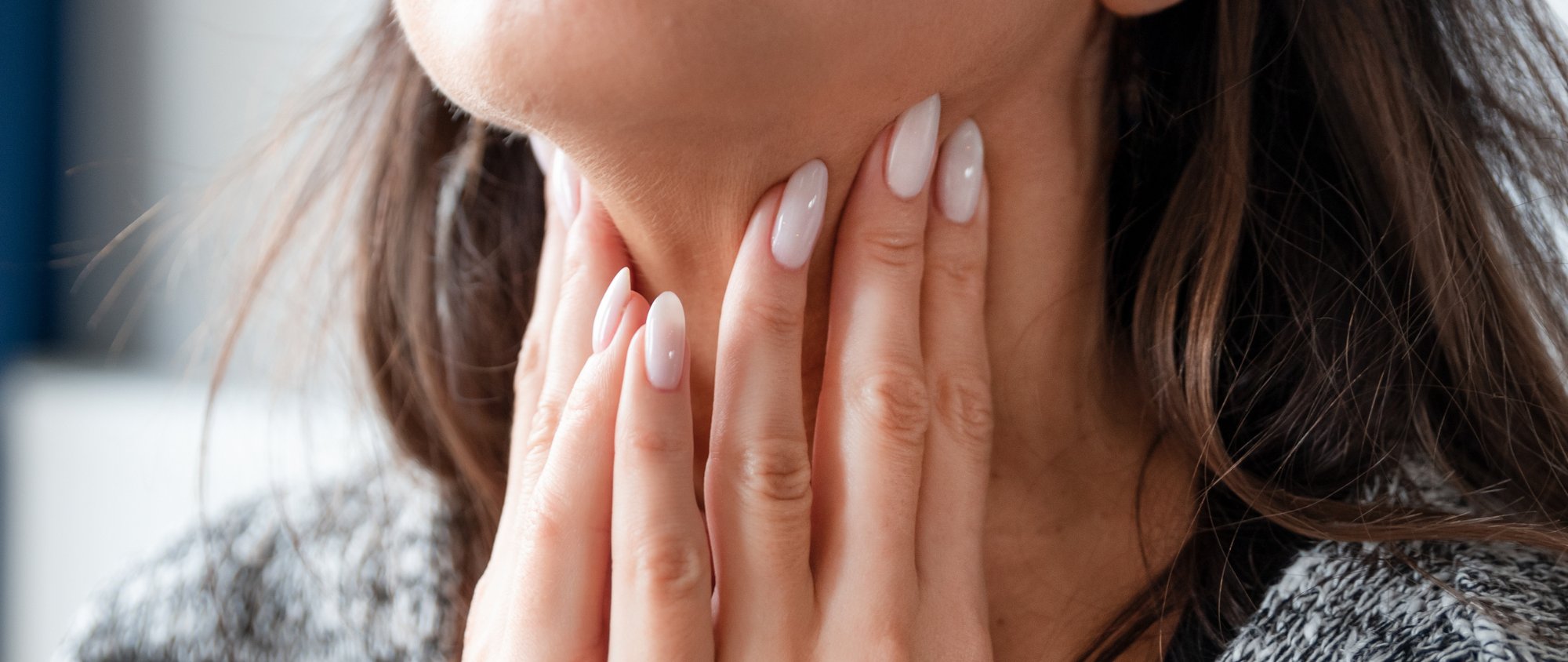 Frau legt beide Hände an ihren Hals.