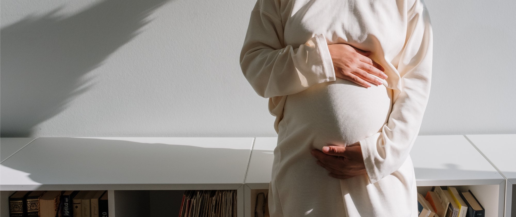 Schwangere Frau hält schützend beide Hände auf ihren Babybauch.